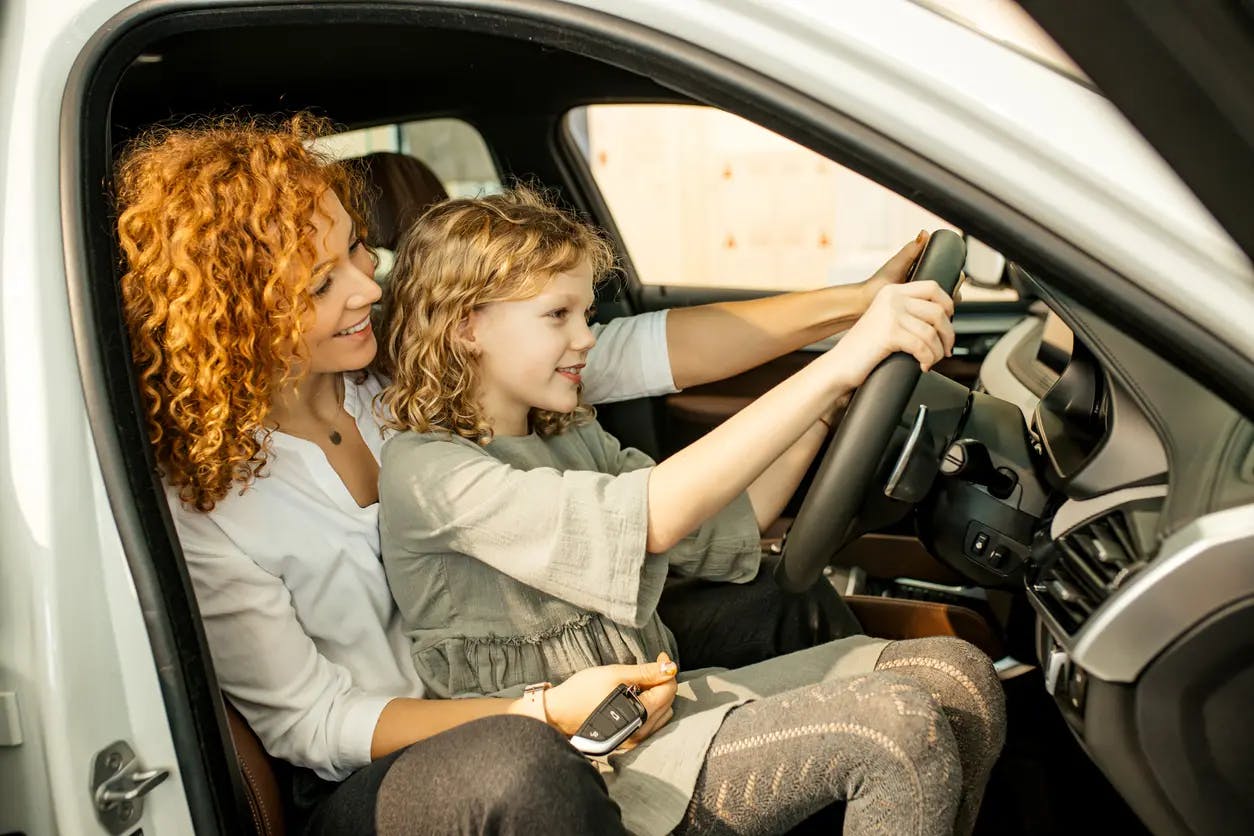 A mother showing her daughter the steering wheel