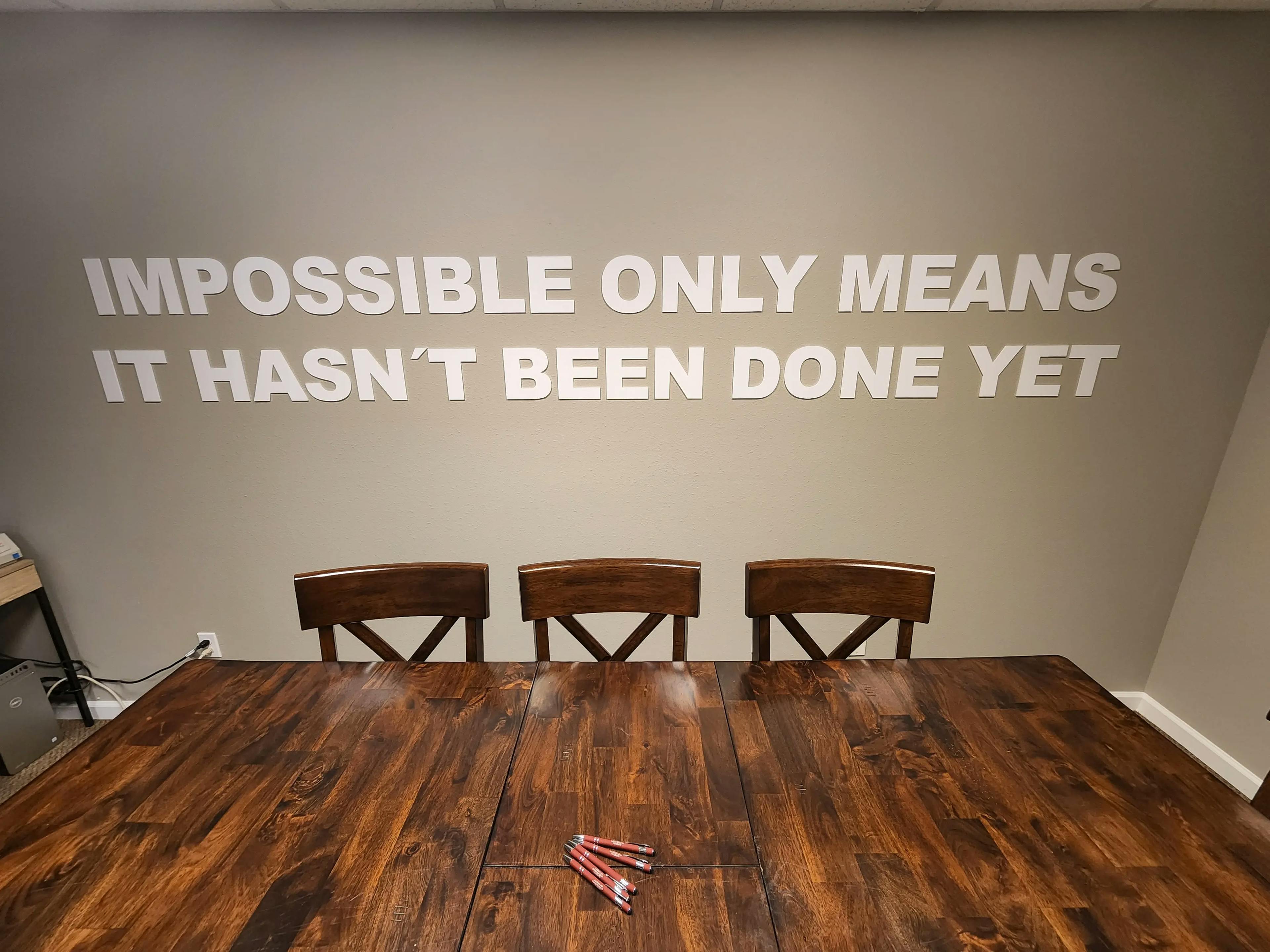 a wooden table with 3 chairs and a quote on the wall